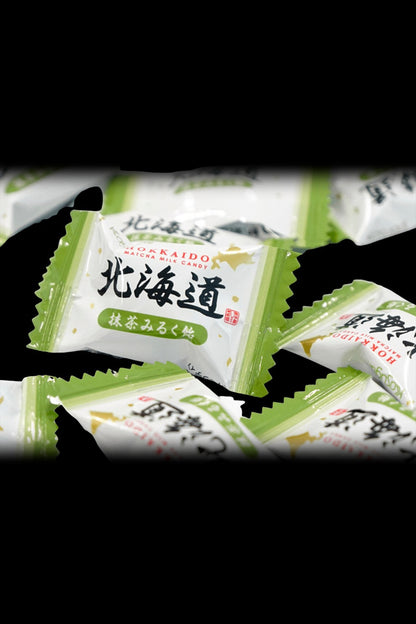 Wrapped, green and white Hokkaido milk candies, possibly infused, displayed on a dark surface.