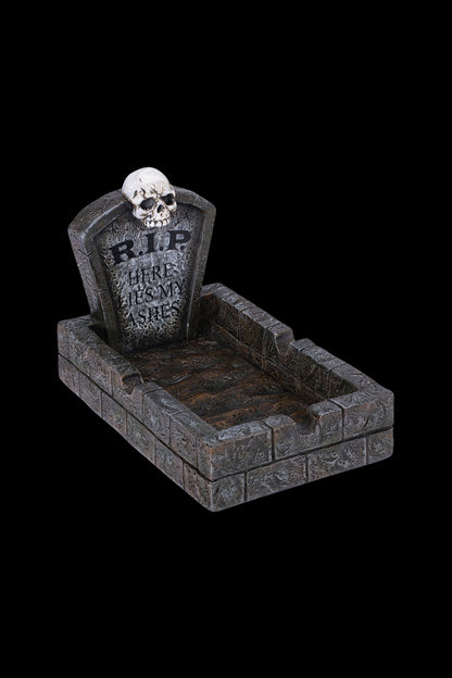 A Halloween-themed ashtray shaped like a graveyard plot, with a skull and "RIP HERE LIES MY ASHES" inscribed on a tombstone.