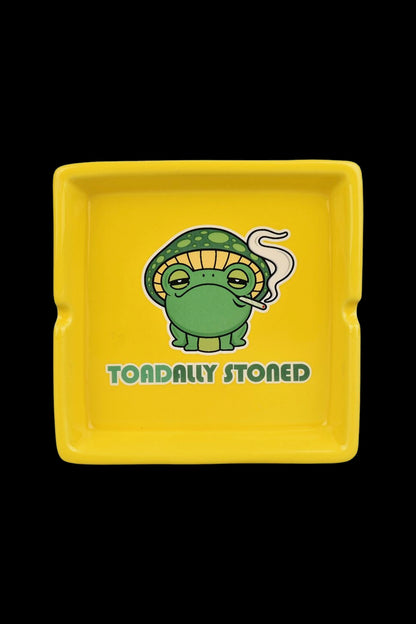 Yellow ashtray featuring a cartoon frog wearing a mushroom cap and exhaling smoke, with the text "TOADALLY STONED."