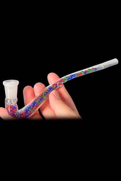 A hand holding a colorful glass pipe for smoking cannabis, against a black background.