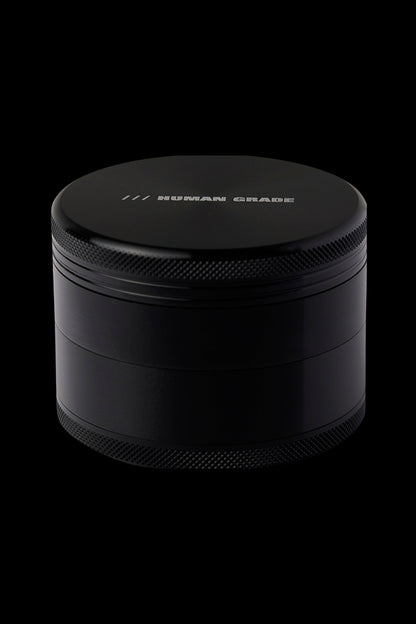 Black four-piece cannabis grinder with “HUMAN GRADE” etched on the lid.