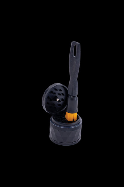 Silver cannabis grinder with open lid and cleaning brush against a black background.