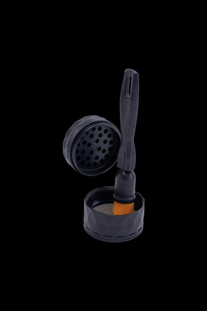 Black cannabis grinder disassembled with cleaning tool on black background.