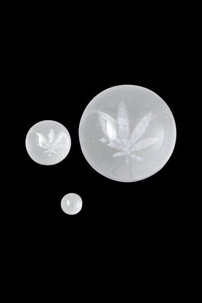 Close-up of three translucent glass bubbles engraved with a leaf motif against black, featuring The Stash Shack Carved Leaf Terp Slurper Set.