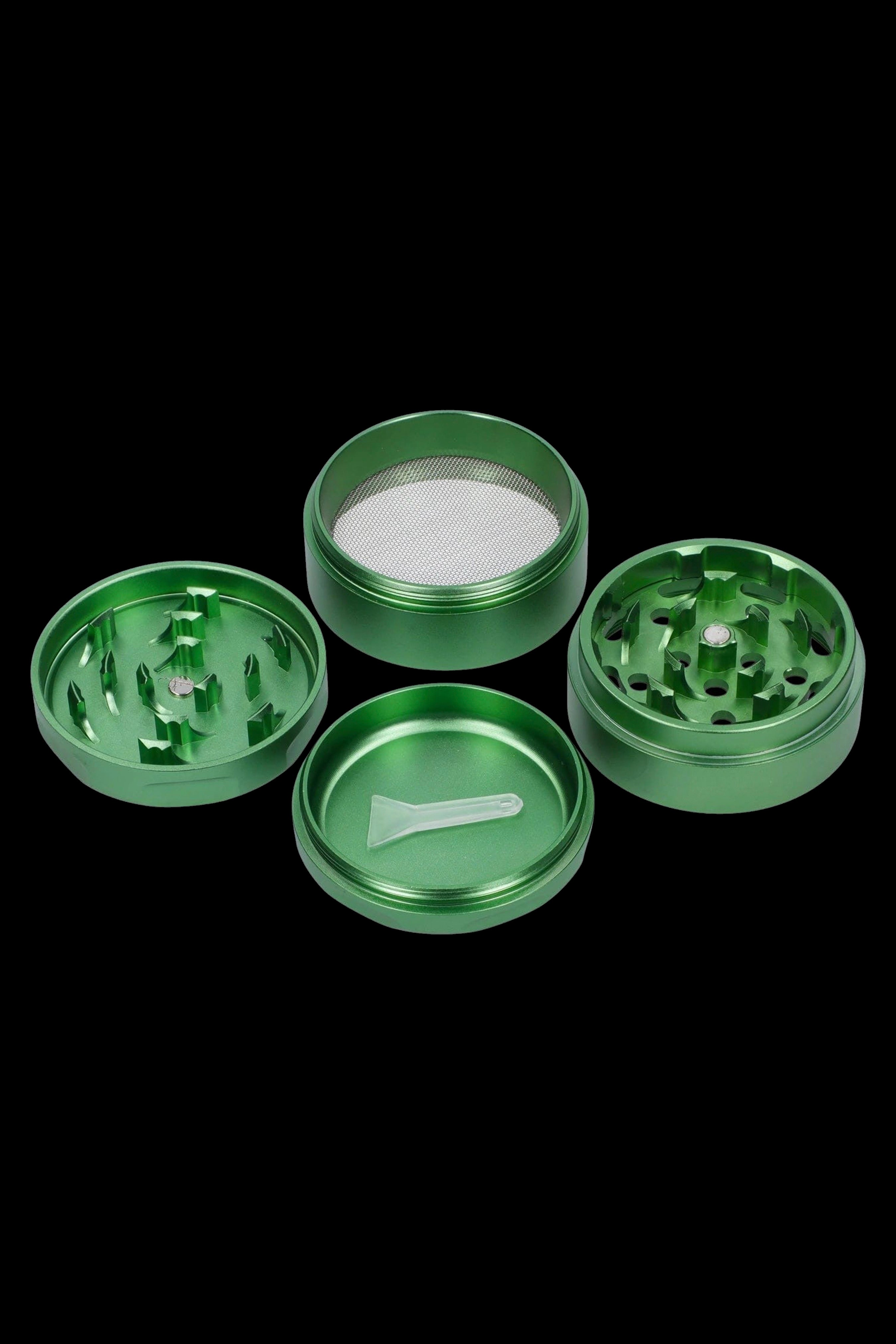 Green four-piece cannabis grinder disassembled, showing the lid, grinding chamber, filter screen, and collection chamber with a small scraping tool.