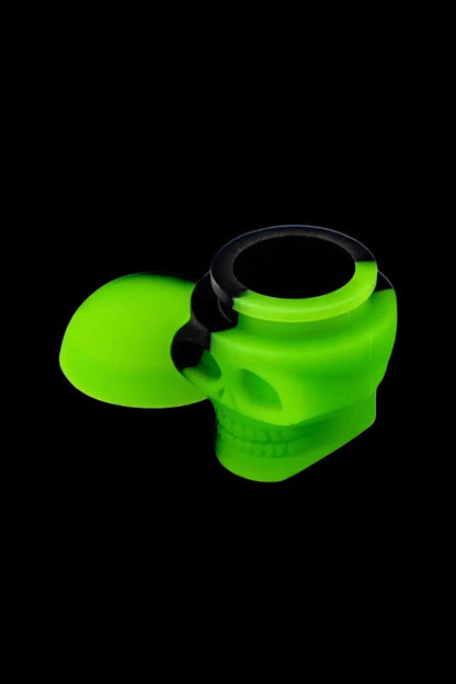 Glowing green skull-shaped silicone bubbler for cannabis smoking against a black background.