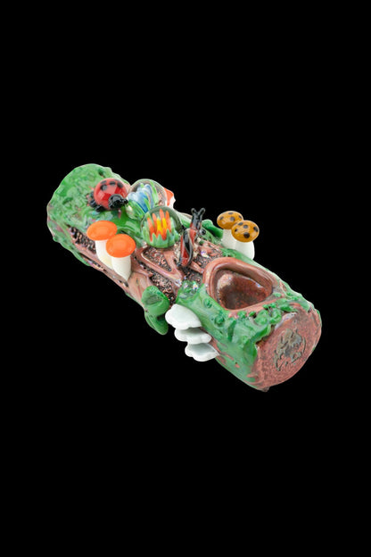 Hand-blown glass pipe sculpted as a whimsical forest log with colorful mushrooms, flowers, and a smiling face.