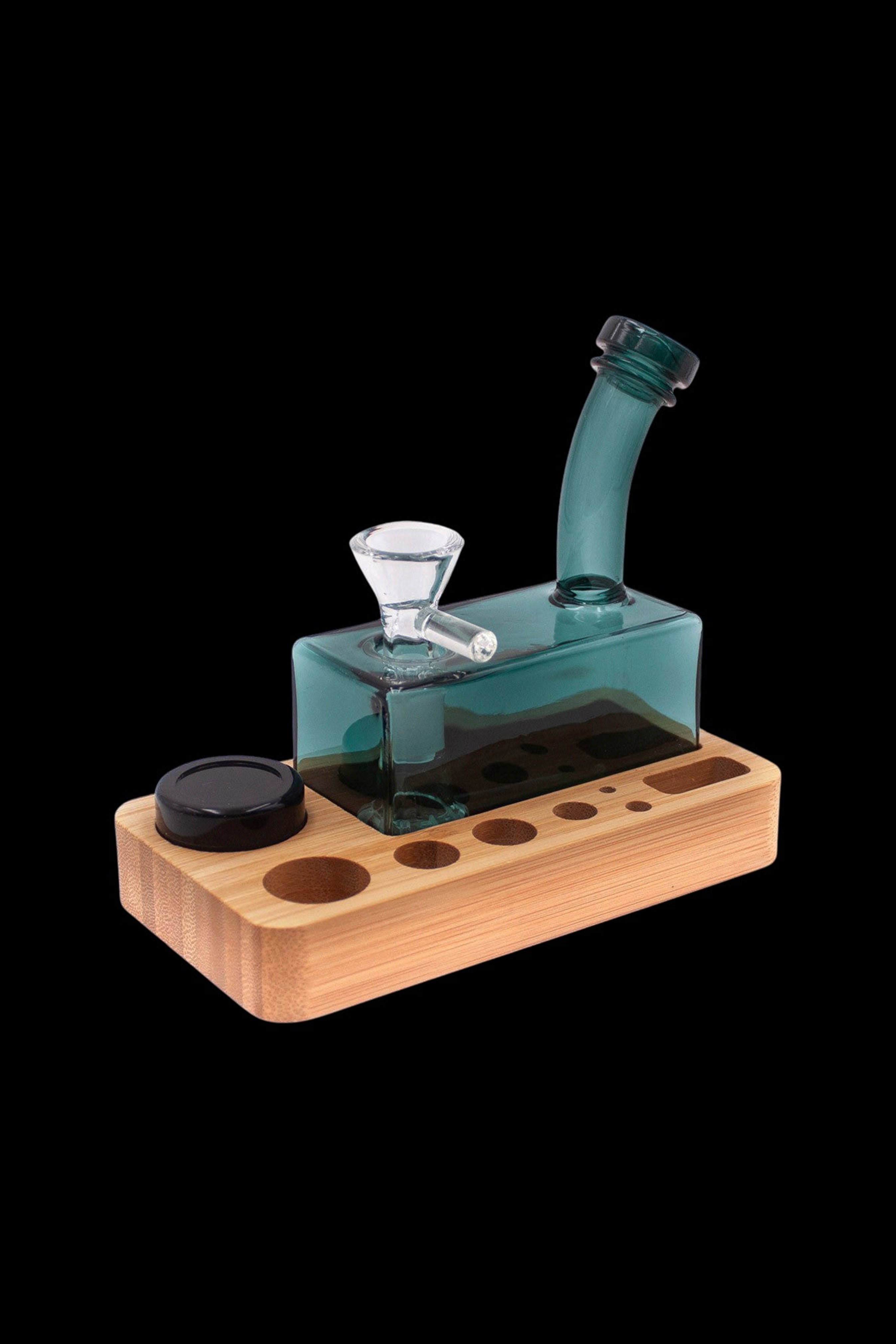 Teal glass water pipe (rig) on a wooden base with storage for accessories.