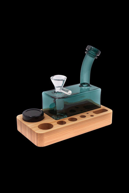 Teal glass water pipe (rig) on a wooden base with storage for accessories.