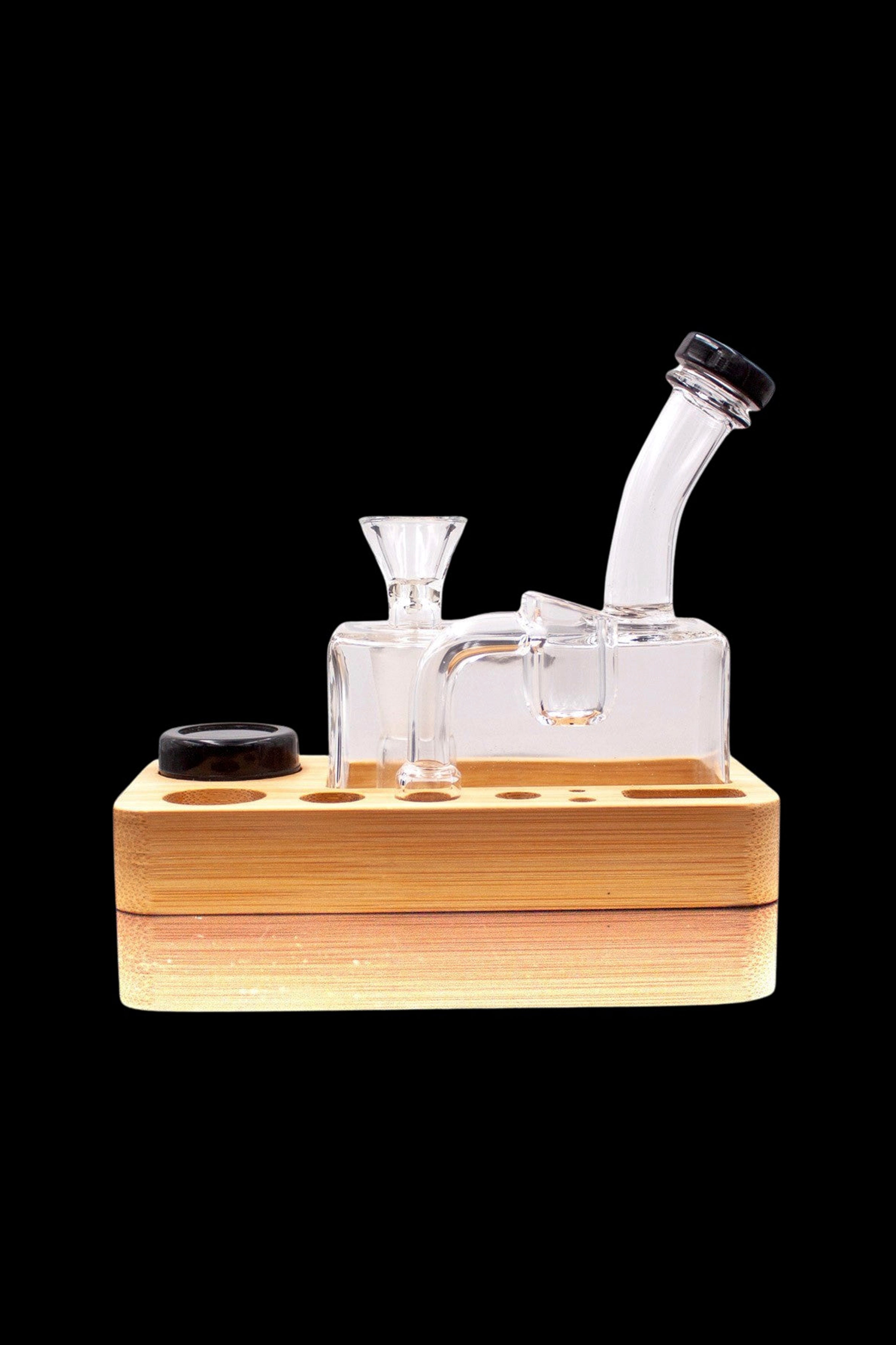 Clear glass dab rig with a wooden base and black carb cap, isolated on a black background.