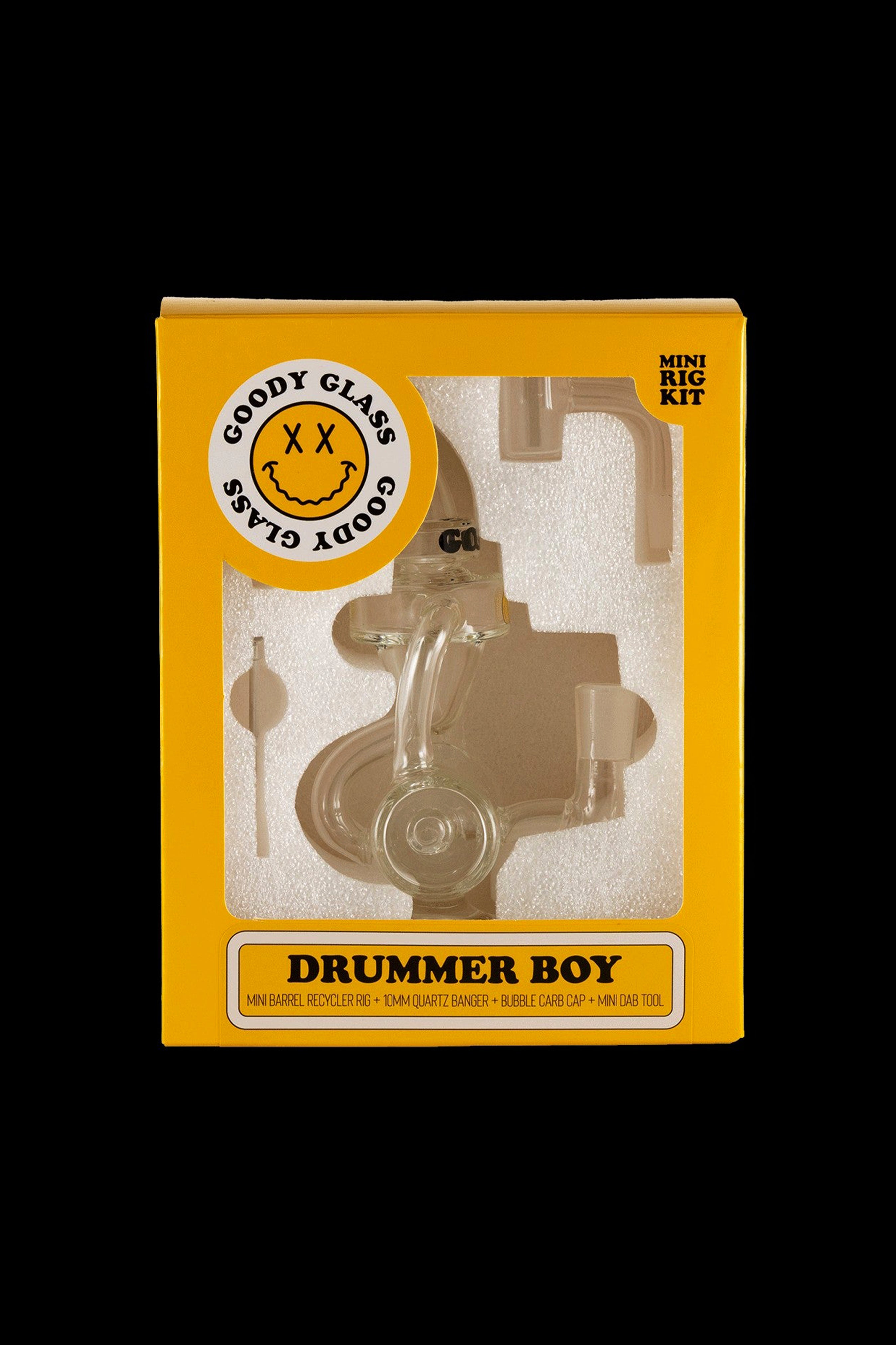 A yellow box for “Goody Glass” branded “Drummer Boy” mini rig kit, featuring a graphic of a small oil rig resembling a drum set and text listing included items: mini barrel recycler rig, 10mm quartz banger, bubble carb cap, and mini dab tool.