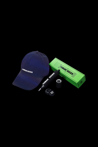 A navy blue baseball cap and green cannabis rolling tray and lanyard, all branded with "HUMAN SUCKS" against a black background.