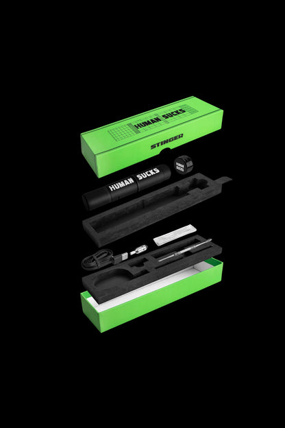 Exploded view of a black cannabis vaporizer kit with neon green packaging displaying the text "Human Sucks" and "Stinger."