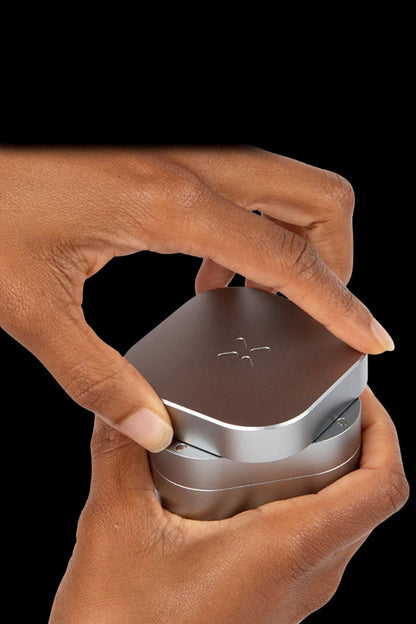 Hands holding a silver cannabis vaporizer against a black background.