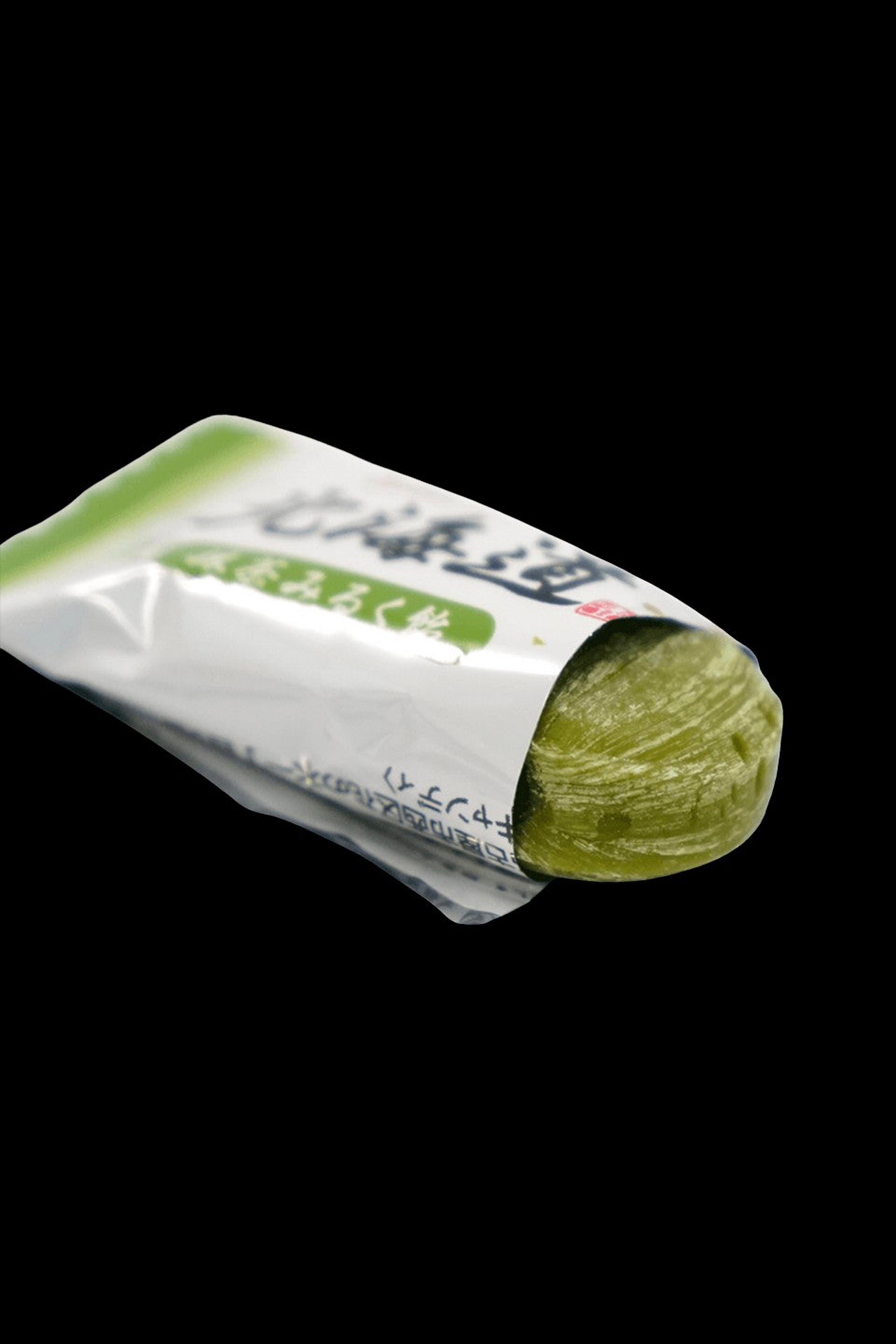 A green cannabis bud partially unwrapped from its packaging, showcasing Japanese text on the wrapper.