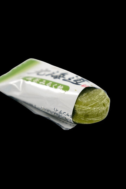 A green cannabis bud partially unwrapped from its packaging, showcasing Japanese text on the wrapper.