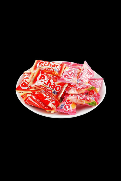 Opened pack of peach-flavored PchaO cannabis drink pouches arranged on a white plate against a black background.