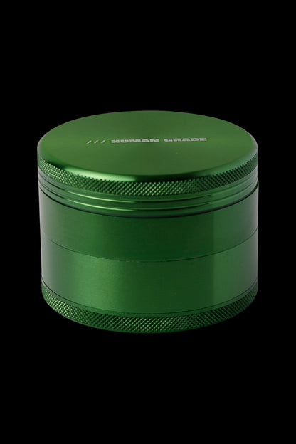 Green four-piece cannabis grinder with "HUMAN GRADE" engraved on the lid.