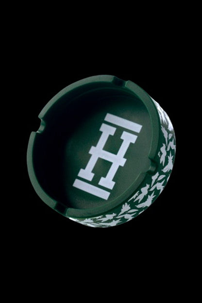 Green cannabis ashtray with a white geometric logo and leaf pattern, isolated on a black background.