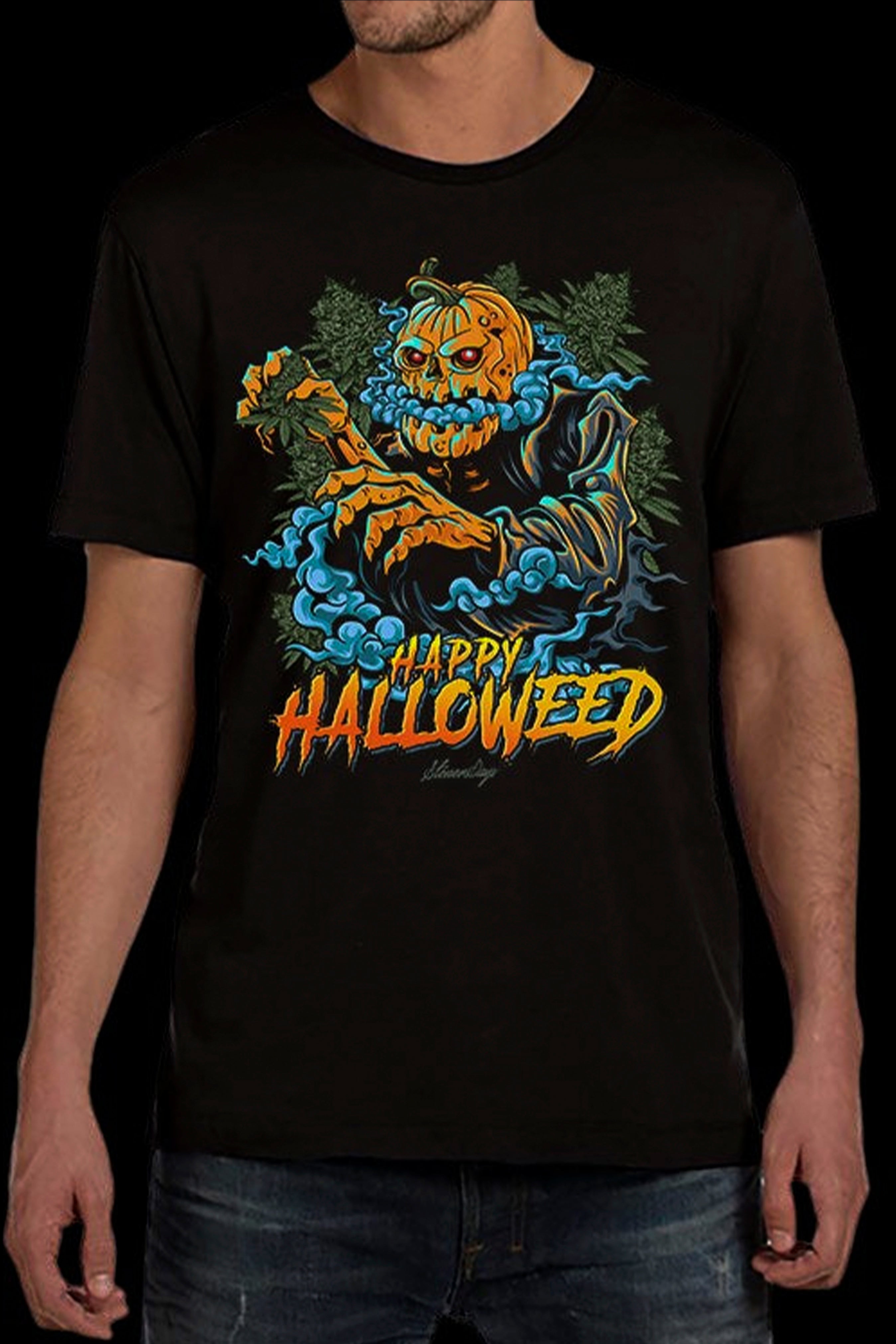 A man wearing a black t-shirt with a colorful graphic design that reads "Happy Halloweed" featuring a spooky pumpkin skeleton surrounded by cannabis leaves and smoke.