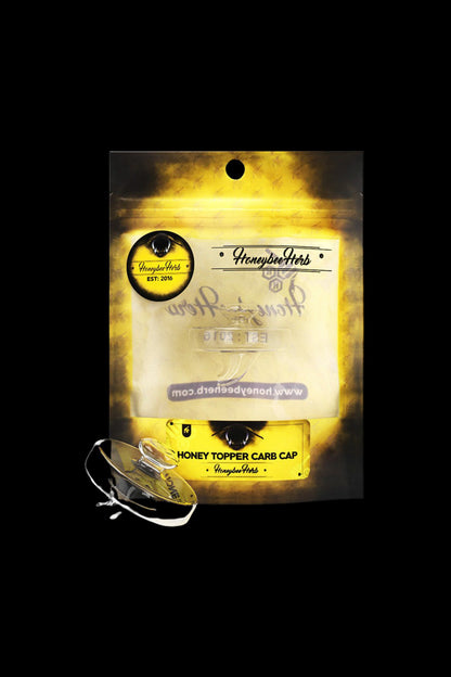 Upside-down view of the Honeybee Herb Honey Topper Carb Cap packaging with a yellow-black label and a clear pink-tinted carb cap in the foreground