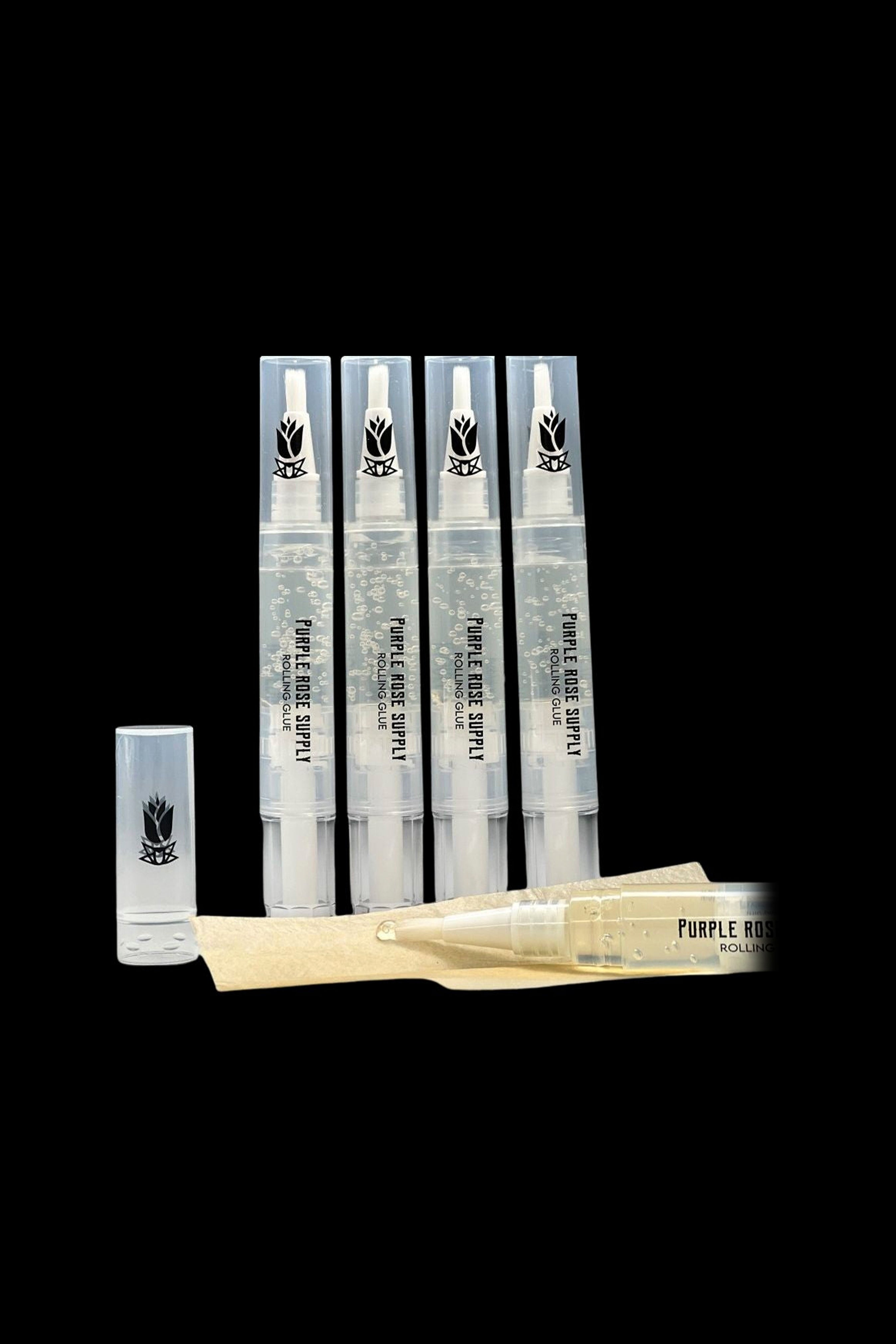 Five clear pen-style tubes of Purple Rose Supply Cannagar & Blunt Rolling Glue stand upright on a black background with one cap off and a brush tip laid horizontally.
