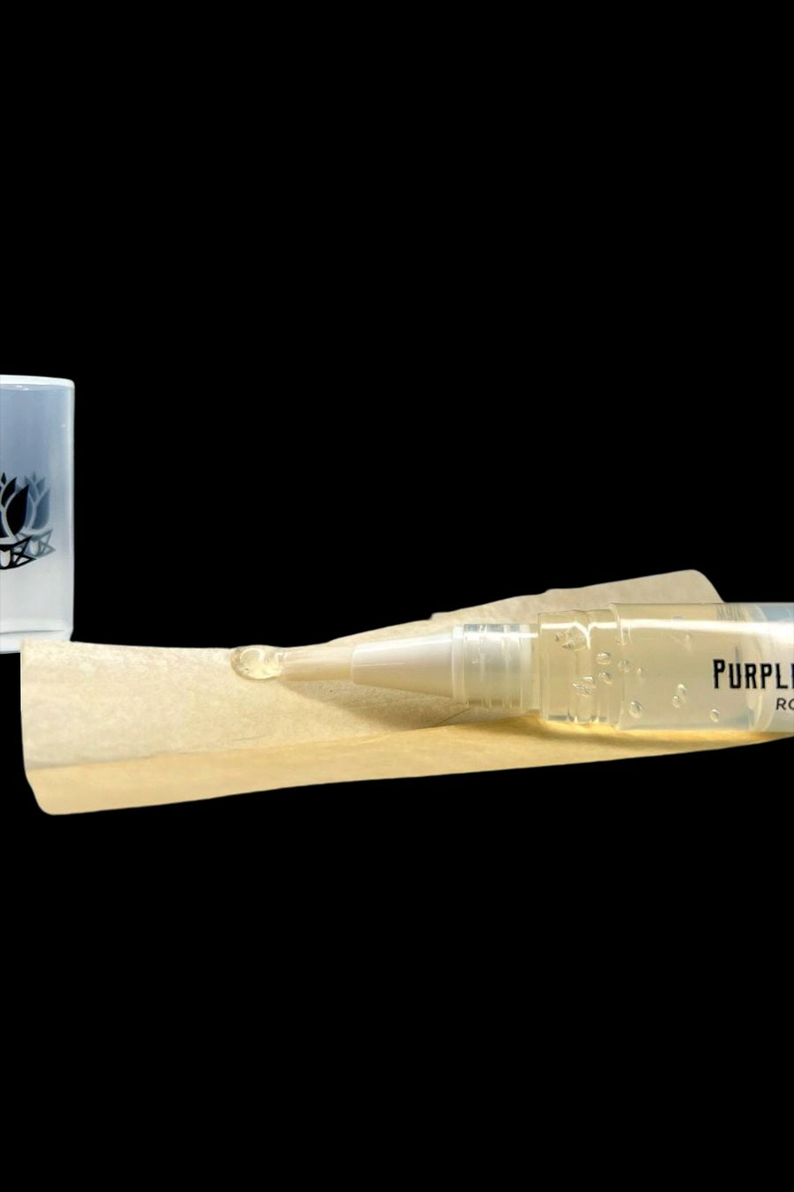 Close-up of a small clear applicator tube of Purple Rose Supply Cannagar & Blunt Rolling Glue resting on a tan rolling paper against a black background