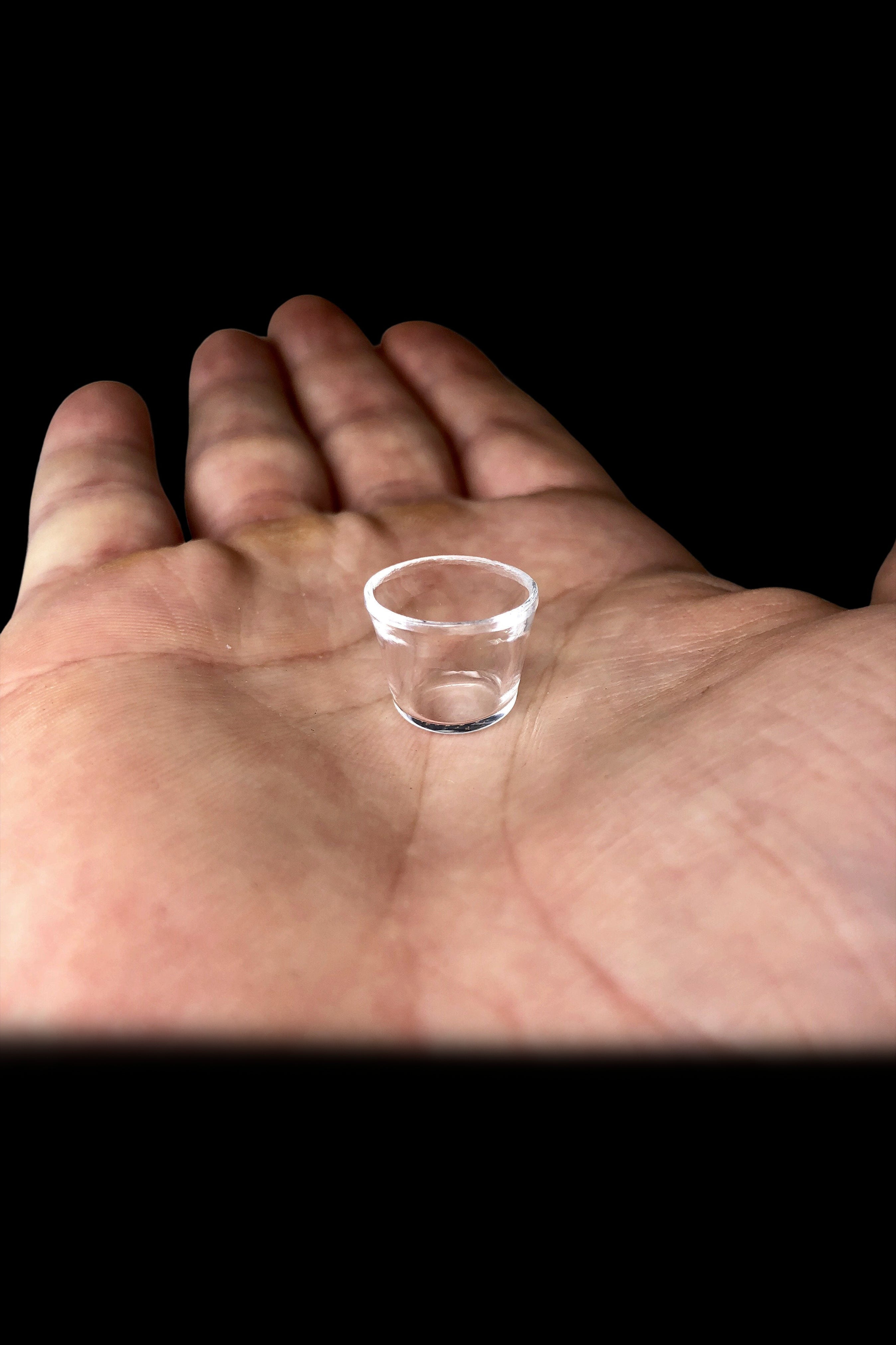 Tiny glass shot cup held in an open palm against a black background.
