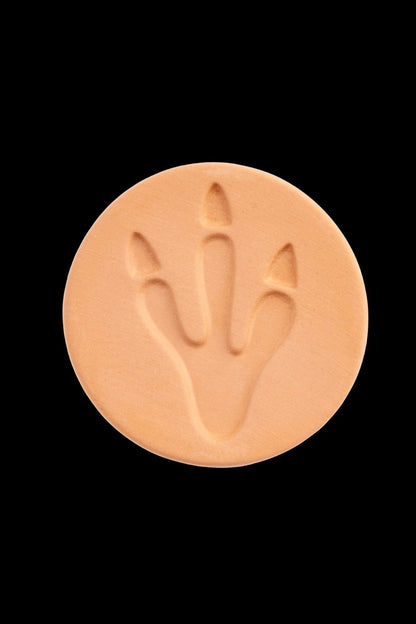 Round, tan cannabis concentrate disc with a stylized, embossed leaf design.