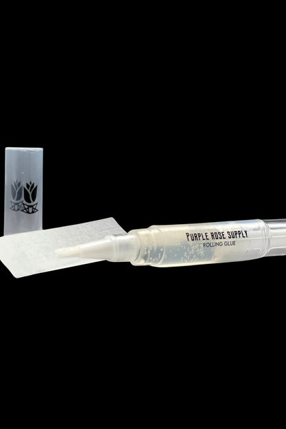 Close-up of the Purple Rose Supply Cannagar & Blunt Rolling Glue pen lying horizontally on black with its white applicator tip and cap visible.