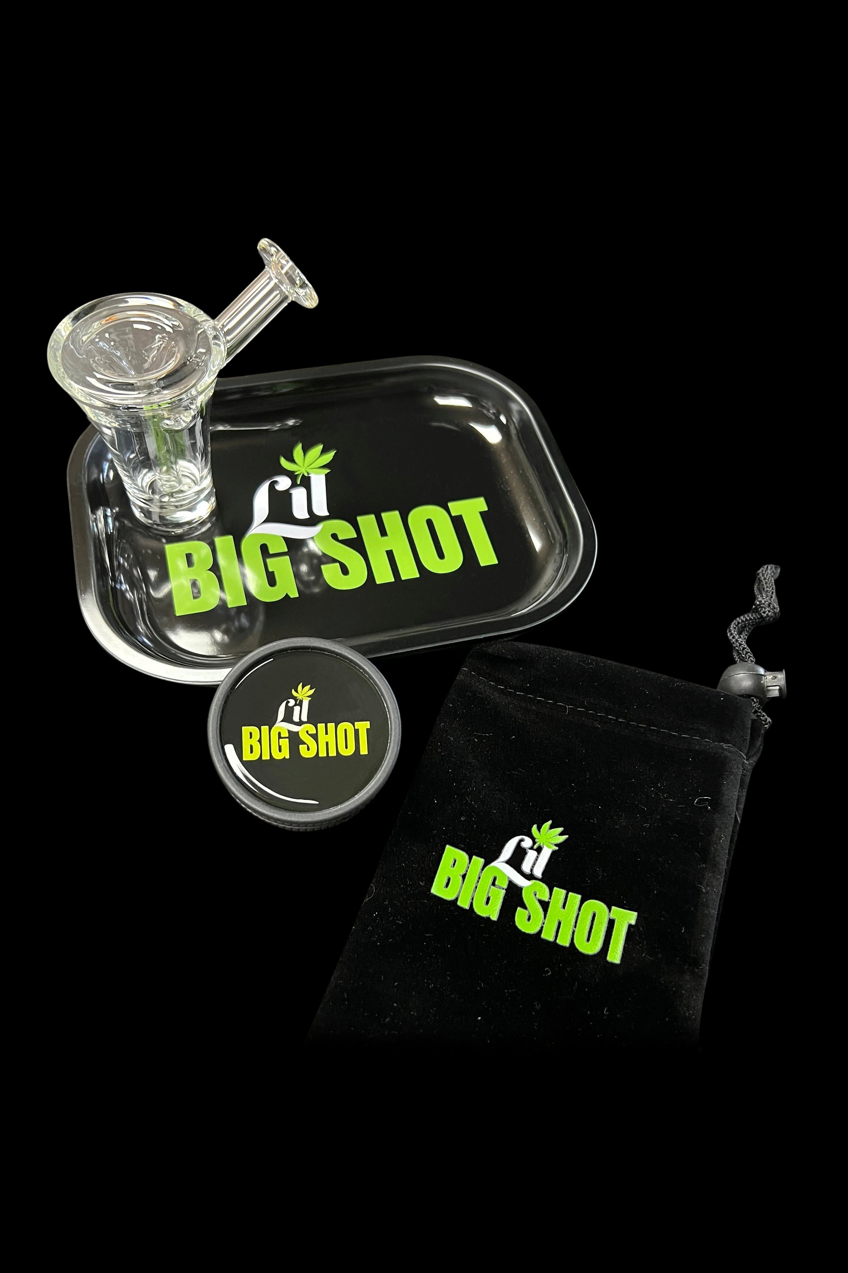 A glass bubbler pipe with a “Big Shot” branded sticker and black drawstring bag, set against a dark background.