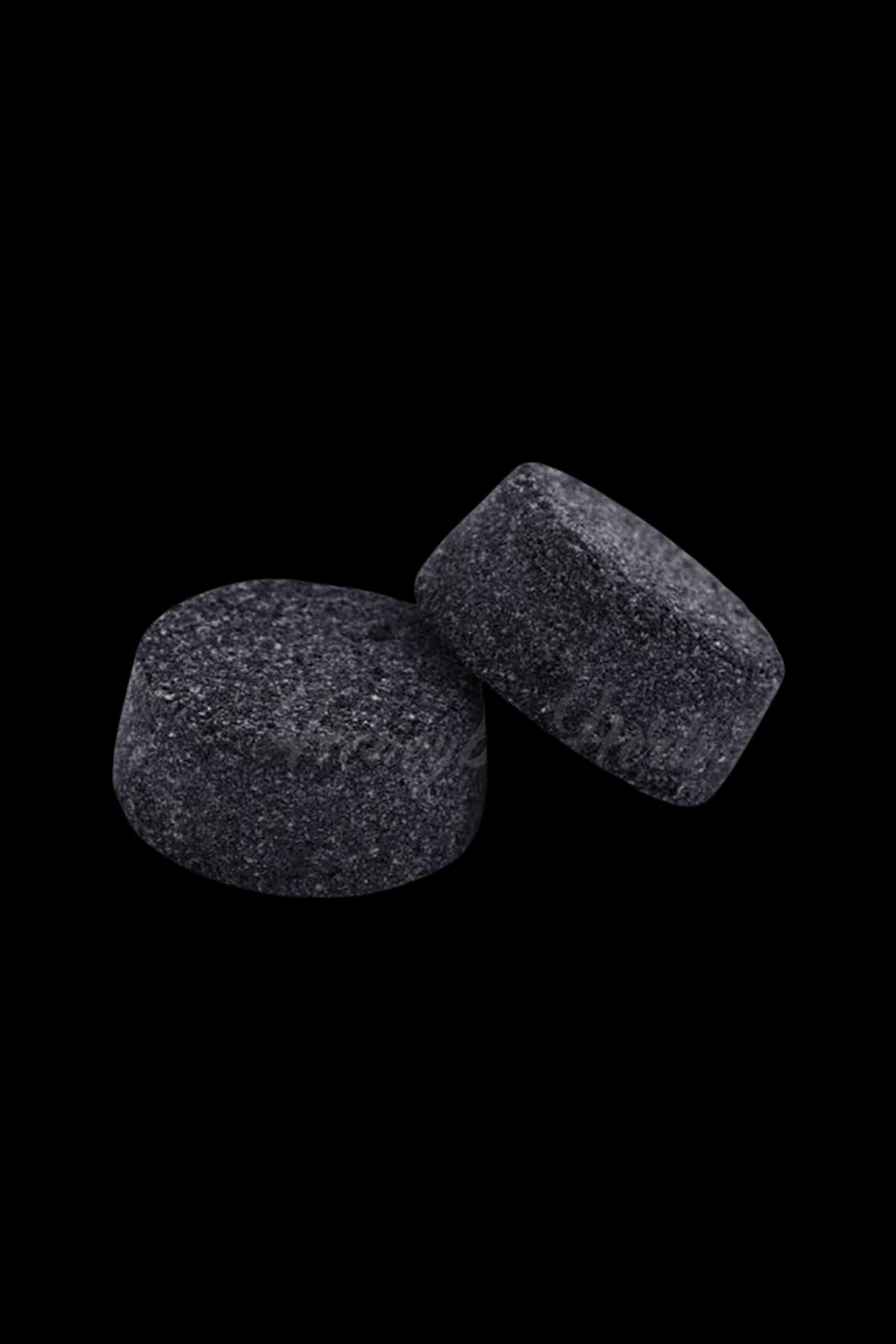 Two dark cannabis hash cubes against a black background.