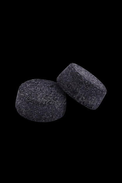 Two dark cannabis hash cubes against a black background.