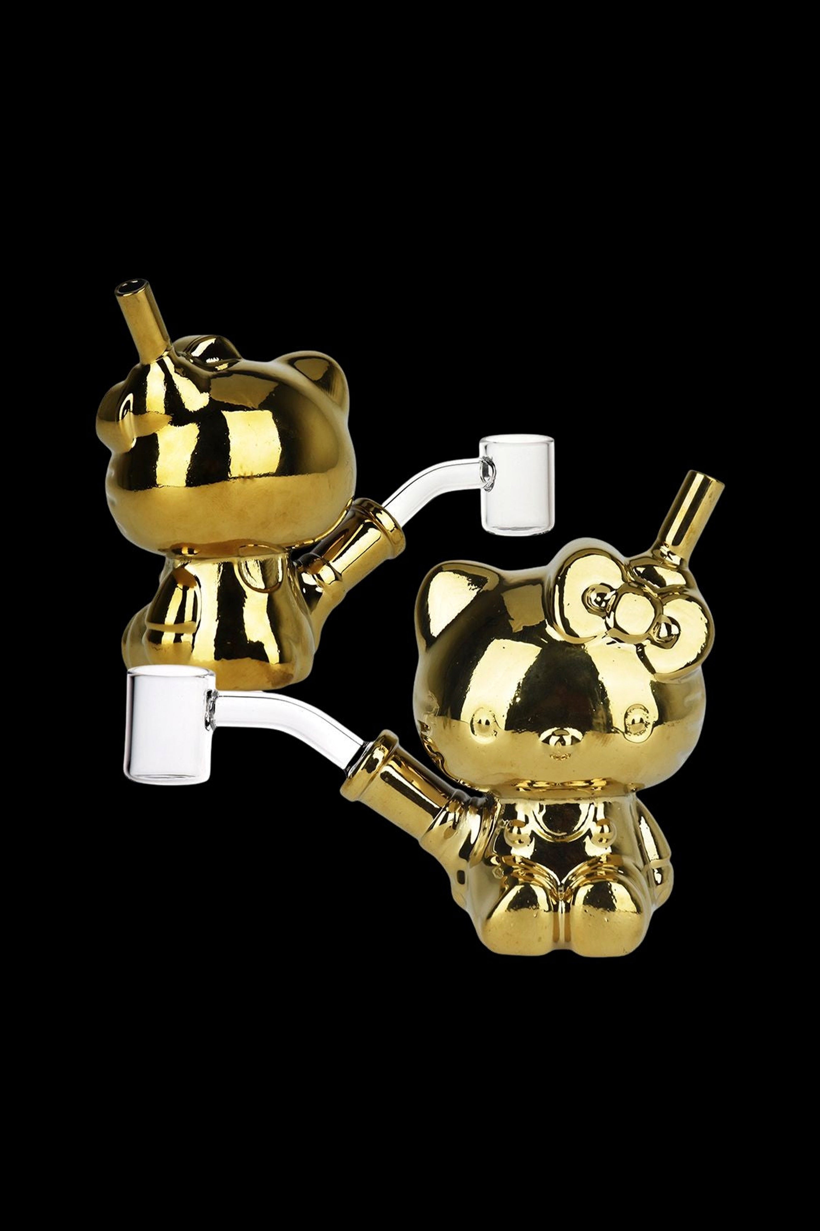 Gold Hello Kitty-shaped cannabis water pipes with clear glass attachments against a black background.