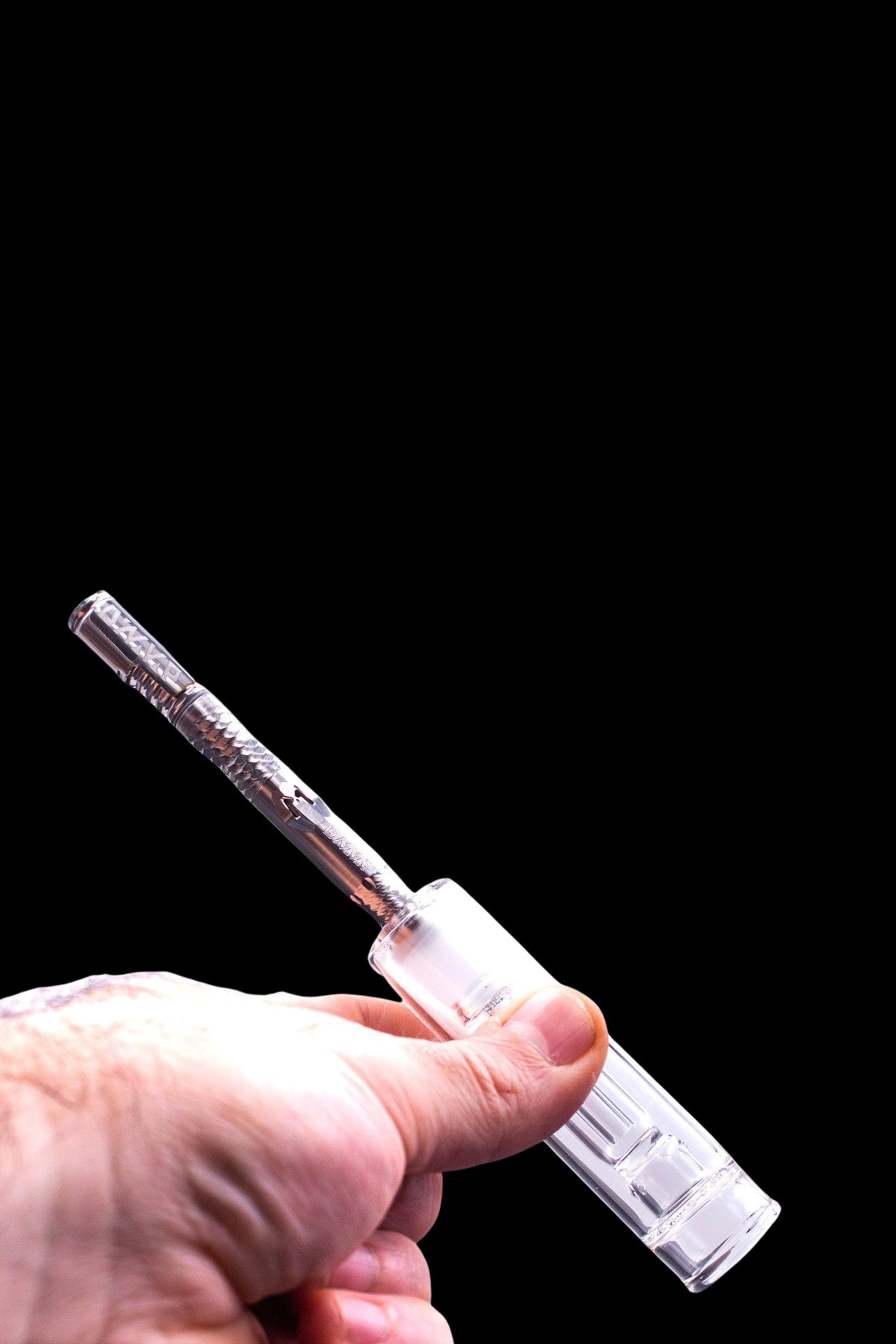 A hand holds a clear glass oil burner pipe against a black background.
