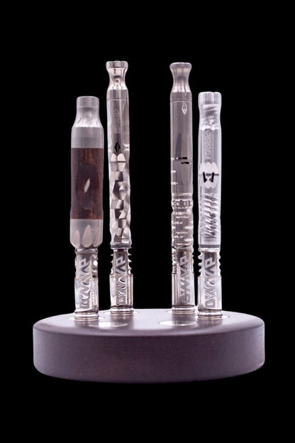 Five glass cannabis oil vape cartridges displayed on a black circular stand, against a dark background.