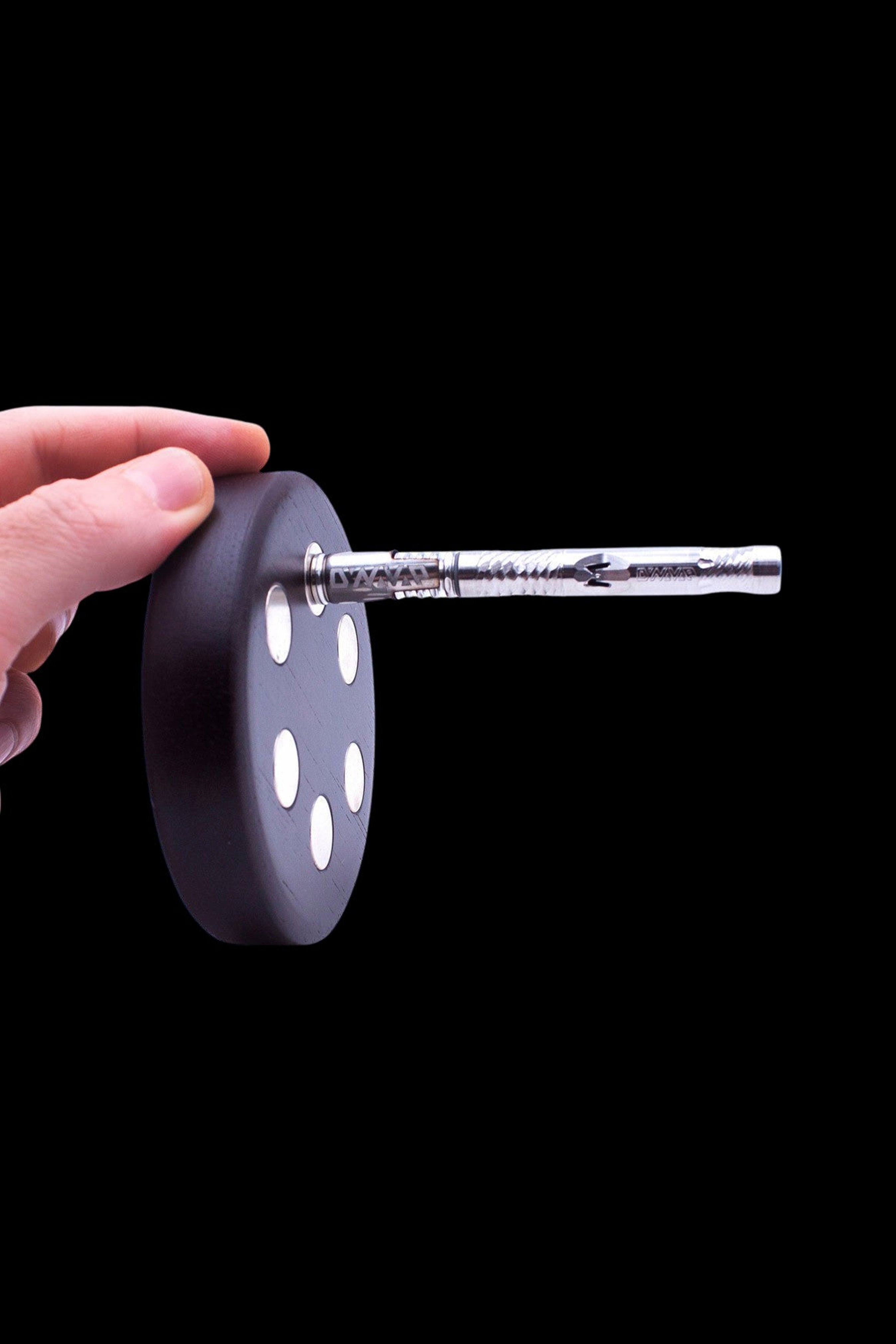 Silver dab straw inserted into a black silicone dab dish held by a hand, against a black background.