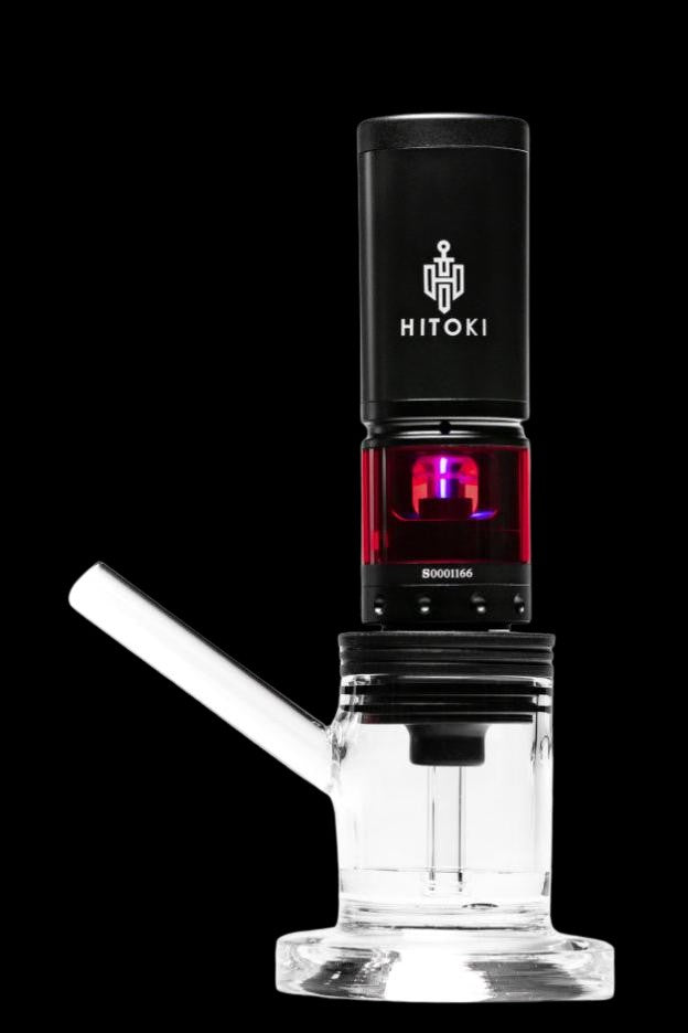 A clear glass water pipe (rig) with a black electronic dab rig insert, displaying a red graphic and branding “HITOKI”.