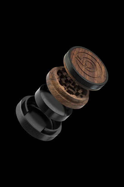 Exploded view of a wooden and black metal cannabis grinder, showcasing its multiple parts suspended in mid-air against a black background.