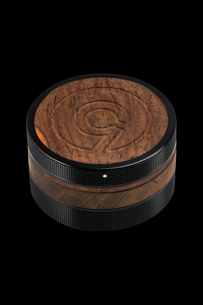 Brown wooden cannabis grinder with textured grip, studio shot on black background.
