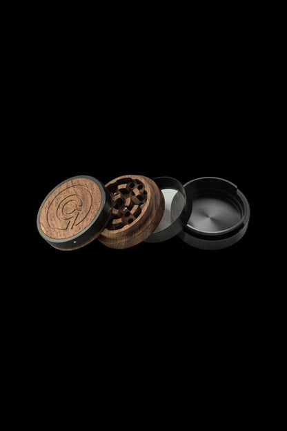 Disassembled wooden and metal cannabis grinder on a black background.