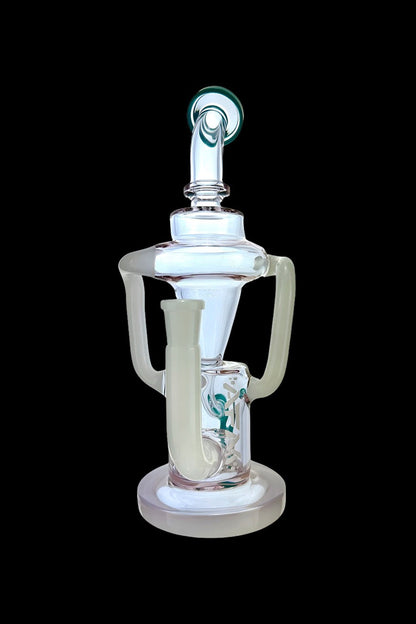 Clear glass dab rig with intricate looping design and green cannabis leaf visible inside, isolated on a black background.
