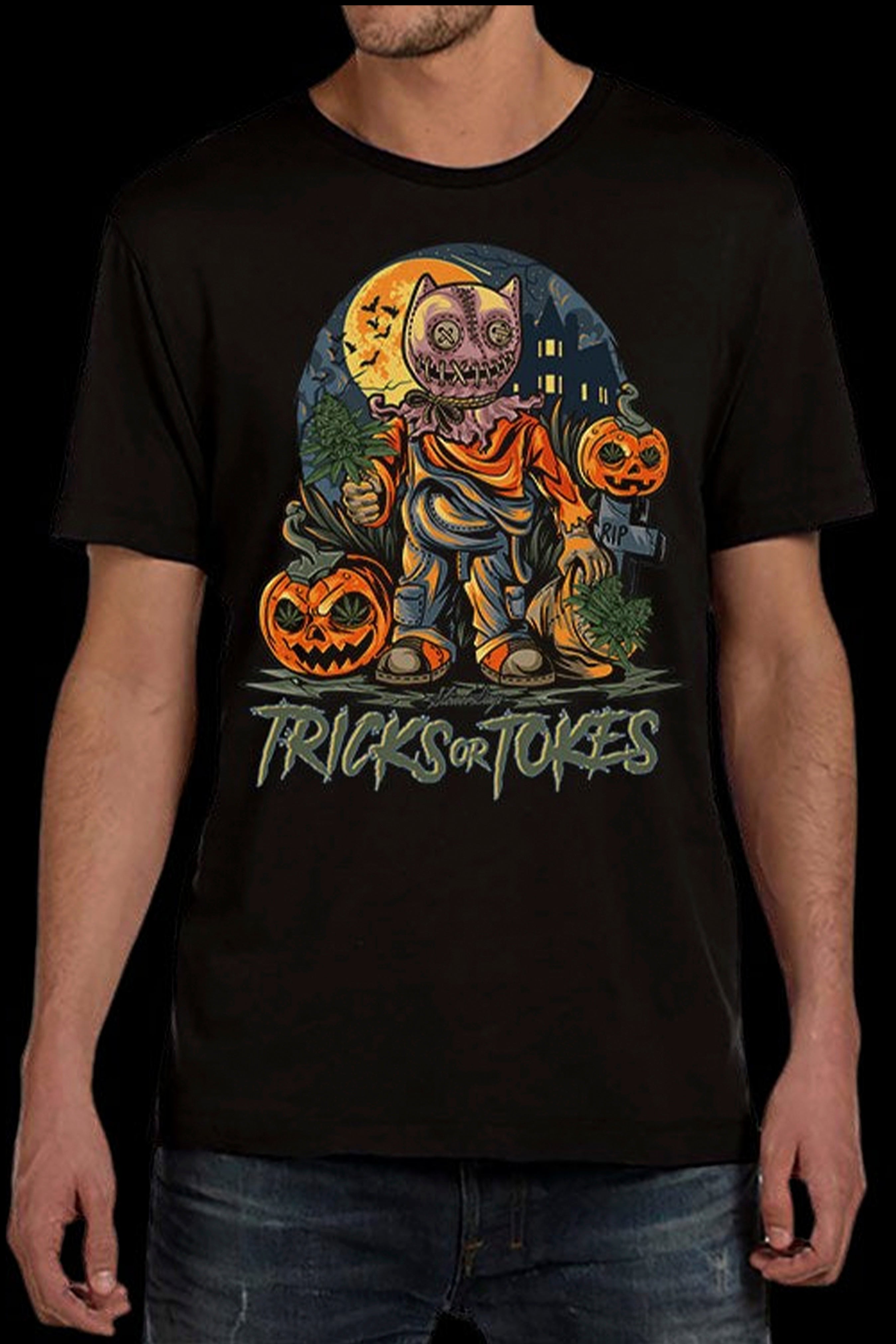 A man wearing a black t-shirt with a colorful Halloween-themed graphic featuring a jack-o'-lantern-headed scarecrow surrounded by pumpkins and foliage, with the text "Trick or Tokes" below.