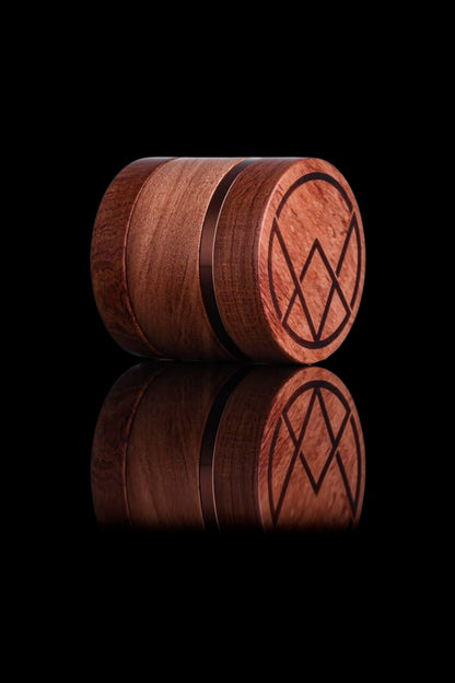 Two wooden cannabis storage jars with geometric designs, reflected on a black surface.
