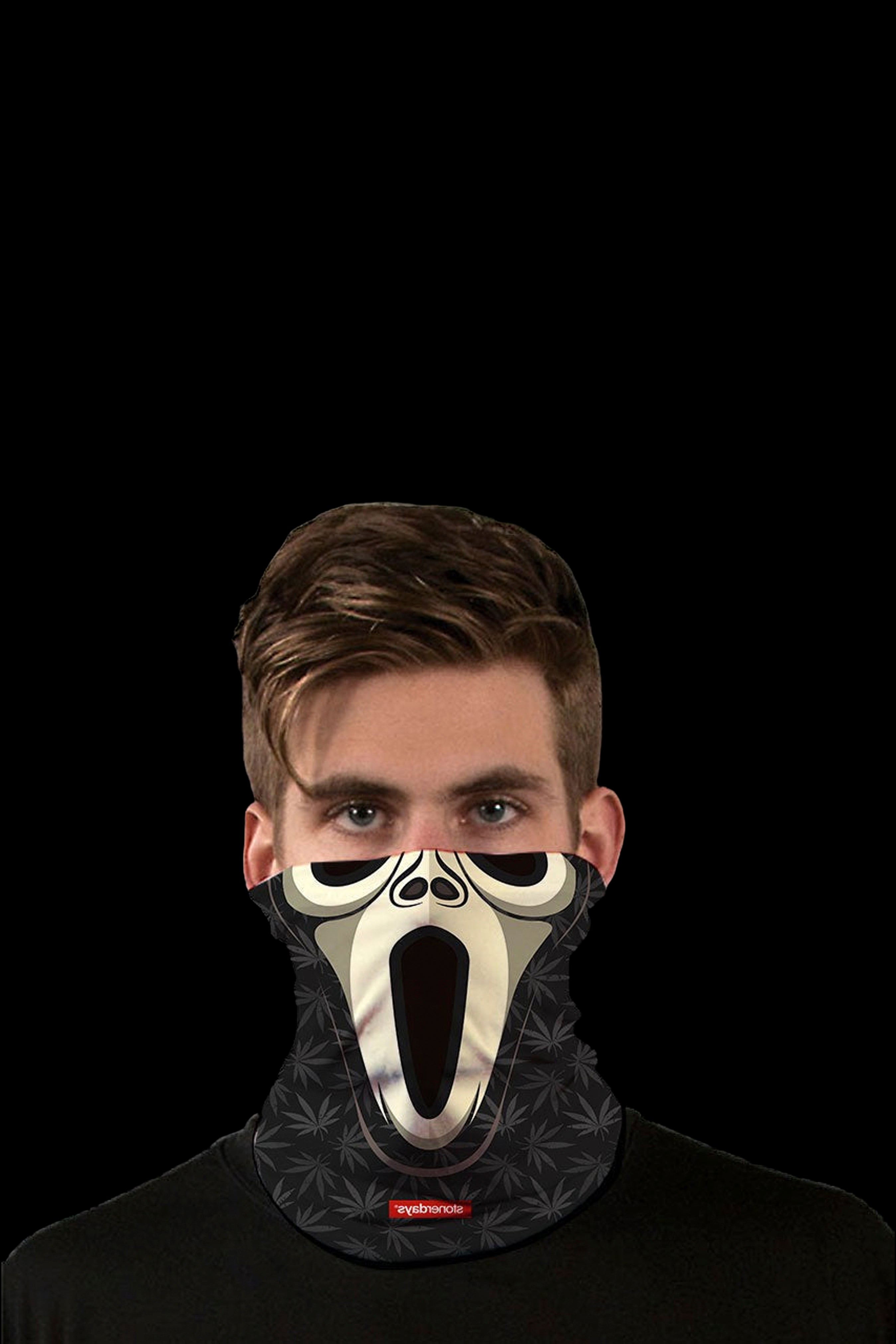 A man wearing a black face mask with a screaming skull design and cannabis leaf pattern, against a black background.