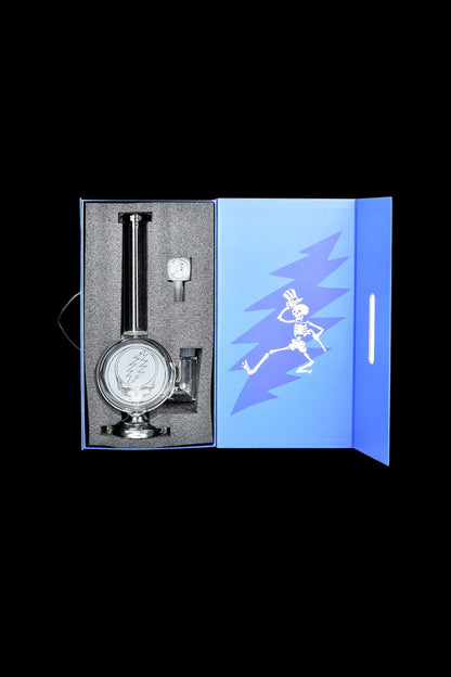 A glass cannabis water pipe, featuring a Steal Your Face skull logo, displayed in an open blue box with a dancing skeleton graphic.