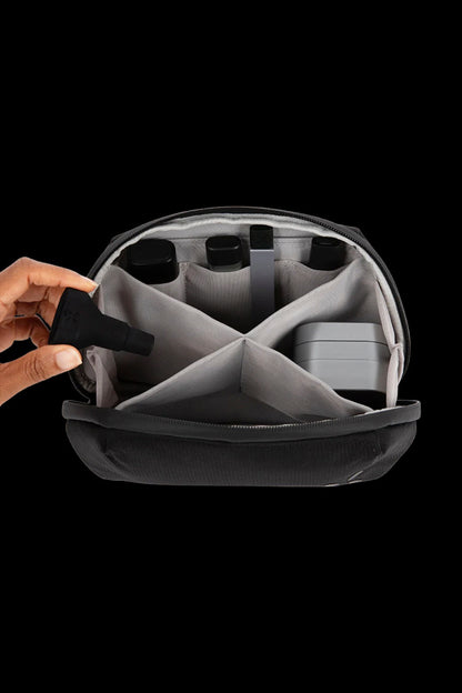 Open cannabis accessories case with organized compartments and a hand reaching for a vape pen.