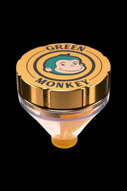 Close-up top-down view of the Green Monkey Patas Grinder showing its gold lid with a smiling green-haired monkey logo against a black background.