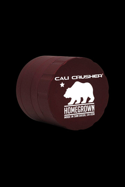 A maroon, circular cannabis grinder labeled “Cali Crusher Homegrown” with a bear graphic and “Made in San Diego, CA USA.”