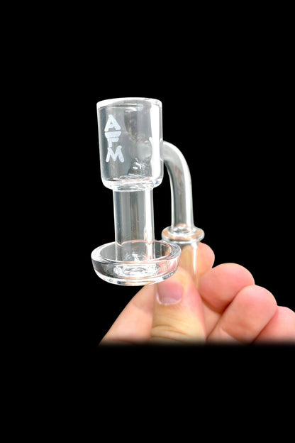 Clear glass dab rig with "ATM" etched on the side, held in a hand against a black background.
